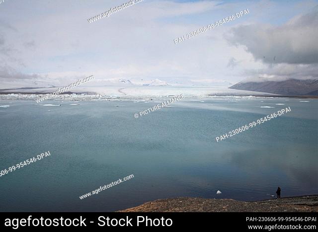 FILED - 12 April 2023, Iceland, Jökulsarlon: A woman stands on the shore of the Icelandic glacial lake Jökulsarlon, while a spur of the Vatnasjökull glacier can...