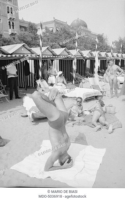Italian actor and basket player Enrico Pagani, on the beach, doing a headstand during the XVIII Venice International Film Festival. Venice, 1957