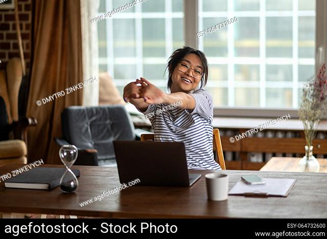 Tired. Tired young asian woman sitting at the laptop and stretching her arms