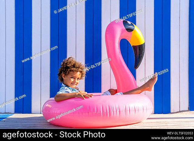 Cute curly haired boy sitting in inflatable flamingo