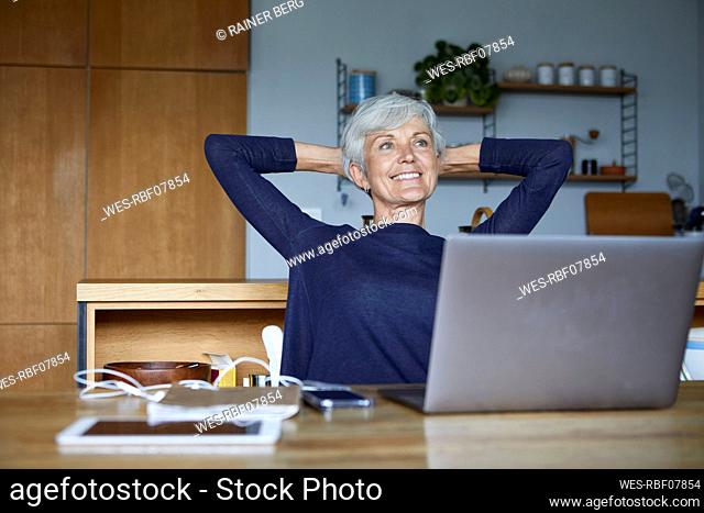 Smiling senior woman with hands behind head relaxing while sitting at home