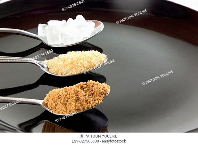 Brown cane sugar and granulated sugar and rock sugar in a metal spoon on the black background. Pure cane sugar for natural