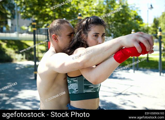 Portrait of young man holding woman from behind, posing a boxing punch, horizontal