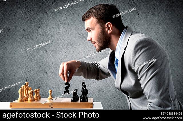 Businessman moving chess figure in chessboard. Successful management and leadership. Handsome man in business suit at desk with chess on grey wall background