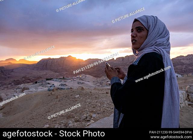 21 November 2021, Jordan, Petra: A Bedouin woman photographs the sunset over the ancient Nabataean city of Petra with a smartphone