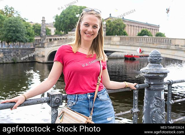 Happy young woman leaning on railing in front of spree river