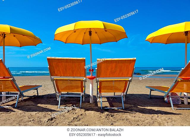 Empty lounge chairs under a yellow umbrella on a deserted beach