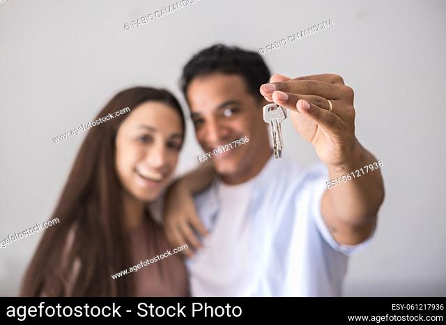 Close up of new home keys and young interracial couple smile and show the property - new life mortage house buyers people concept - happy youth family in love...