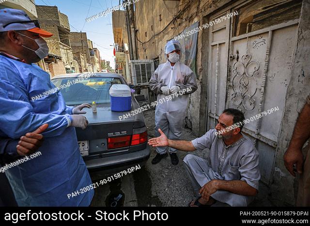 21 May 2020, Iraq, Baghdad: Health workers of the Ministry of Health wearing protective suits speak with a man during a field examination to perform coronavirus...