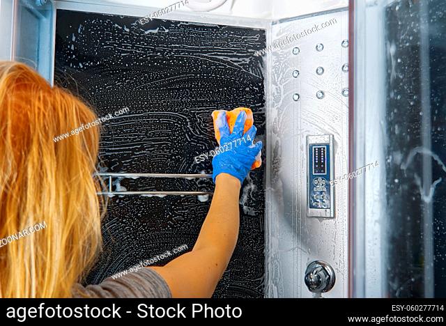 Cleaning of shower steam cabins from Calcium deposits. Cleaning in the bathroom. woman hand in blue gloves with rag and detergent