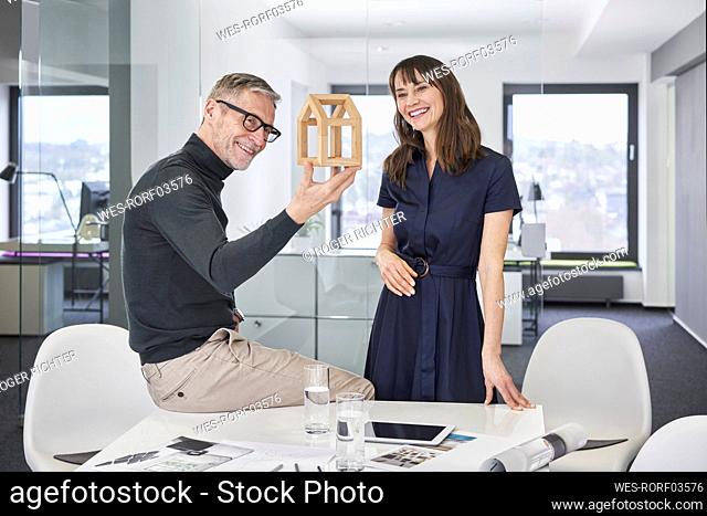 Two smiling architects looking at model house in office