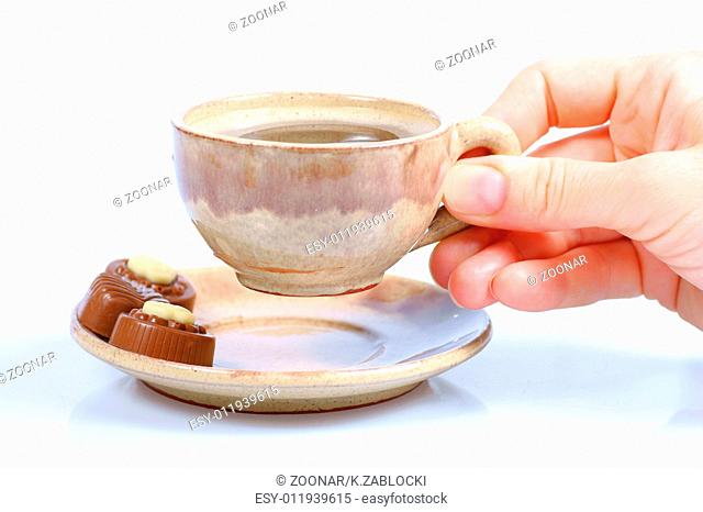 chocolate pralines, cup, black coffee and female hand on white