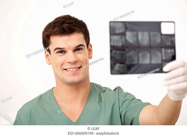 A smiling happy dentist holding x-rays, looking at the camera