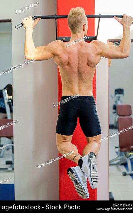 Blond, attractive young man hanging from gym equipment, seen from the back