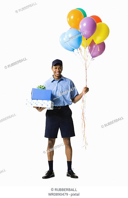 Young man carrying gift boxes while holding balloons