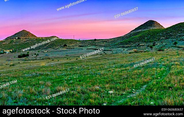 Colorful sunset in picturesque countryside in Andalusia with fields and a hiking trail leading to distant hills