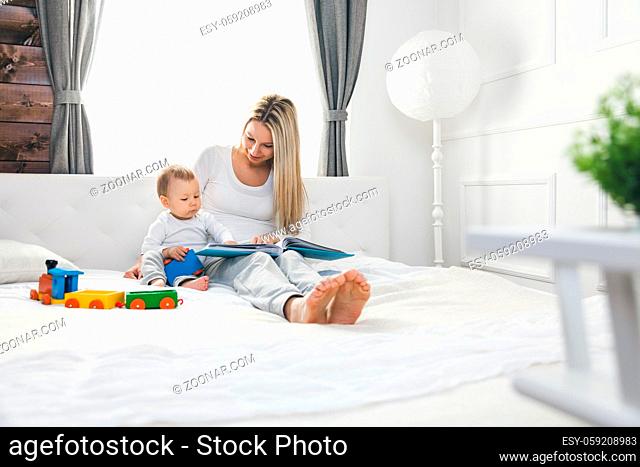 Child education. Happy mother with her toddler sitting on the bed and reading a book together