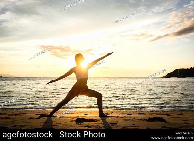 Full length side view of the silhouette of a fit woman practicing the warrior yoga pose against sky at sunset during summer vacation in Flores Island, Indonesia