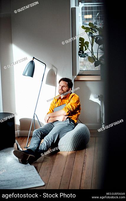 Businessman with digital tablet sitting on hassock in office