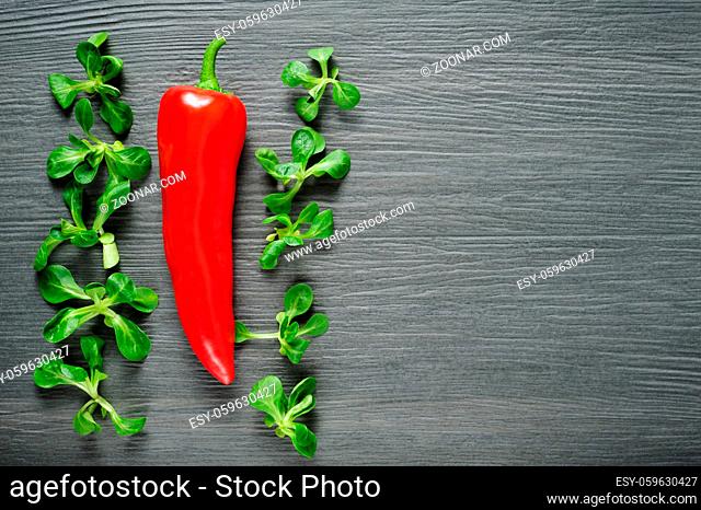 One ripe sweet red Kapia pepper with valeriana salad leaves on dark shale stone background
