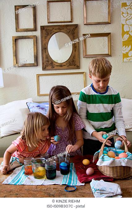 Boy and two sisters dyeing easter eggs in jars at table