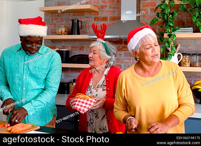 Three diverse senior male and female friends in christmas hats cooking together in kitchen