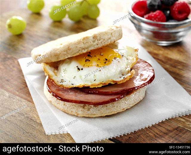 Canadian Bacon and fried egg breakfast sandwich on an English Muffin with fruits
