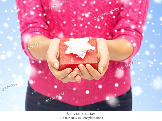 christmas, holidays and people concept - close up of woman in pink sweater holding small red gift box over blue background with snow over blue background with...