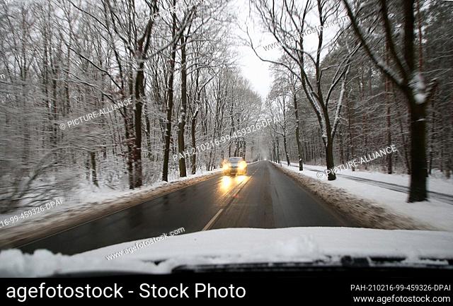 16 February 2021, Berlin: A car drives through a snow-covered road. Fresh snow from last night and glassy roads are causing obstructions in the morning rush...