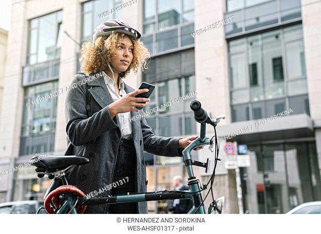 Woman with bicycle and smartphone in the city, Berlin, Germany