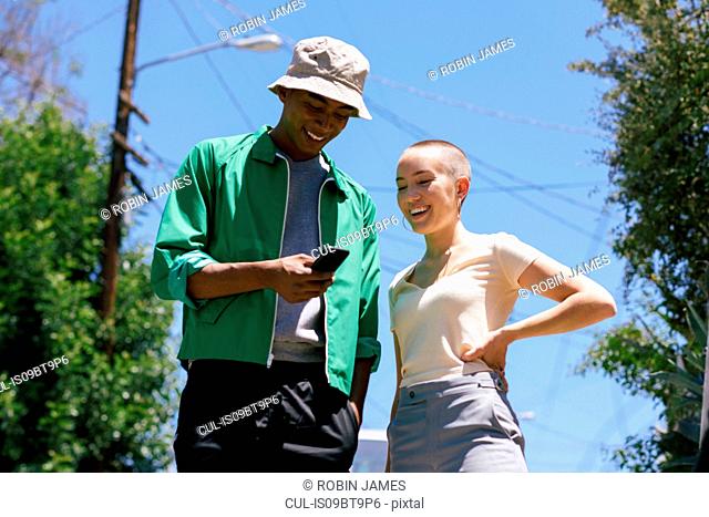 Young man and female friend looking at smartphone in suburbs, Los Angeles, California, USA
