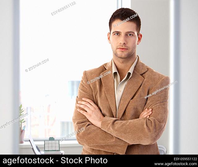 Casual office worker standing arms crossed in bright office