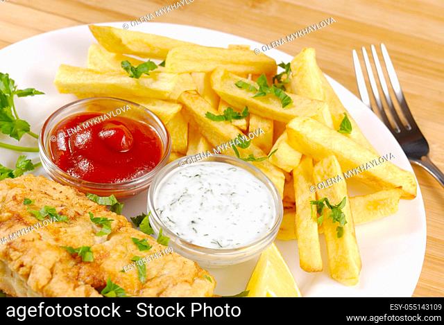 White plate with fish and chips, mayo, lemon and ketchup
