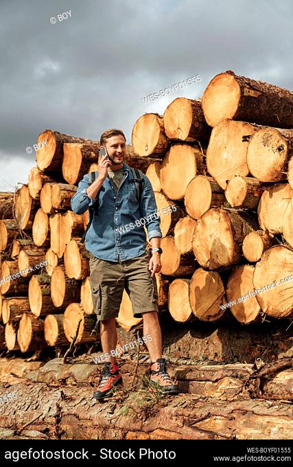 Mid adult man talking over smart phone while standing by woodpile in forest