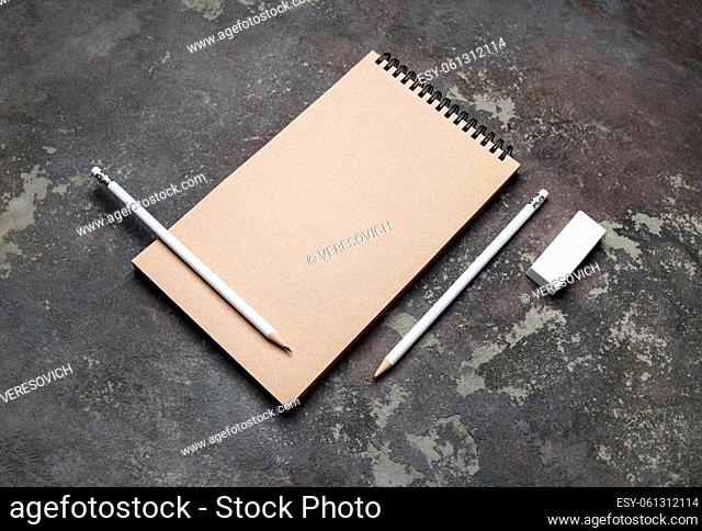 Photo of closed blank kraft sketchbook, pencils and eraser on concrete background. Stationery template