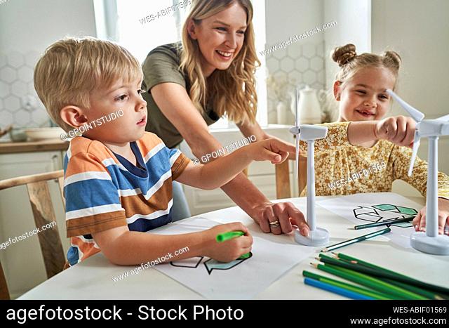 Mother explaining wind turbine model to children at home