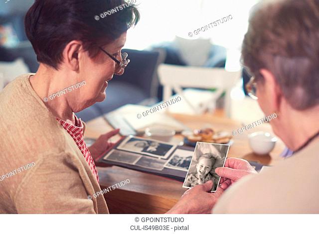 Over shoulder view of two senior women looking at old photographs at table