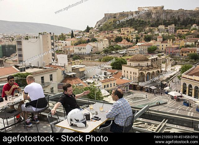 03 May 2021, Greece, Athen: Guests sit in a café in the Monastiraki district with the Acropolis in the background. Greece is easing the measures imposed because...