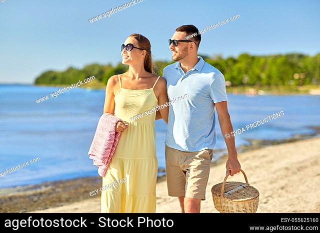 happy couple with picnic basket walking on beach