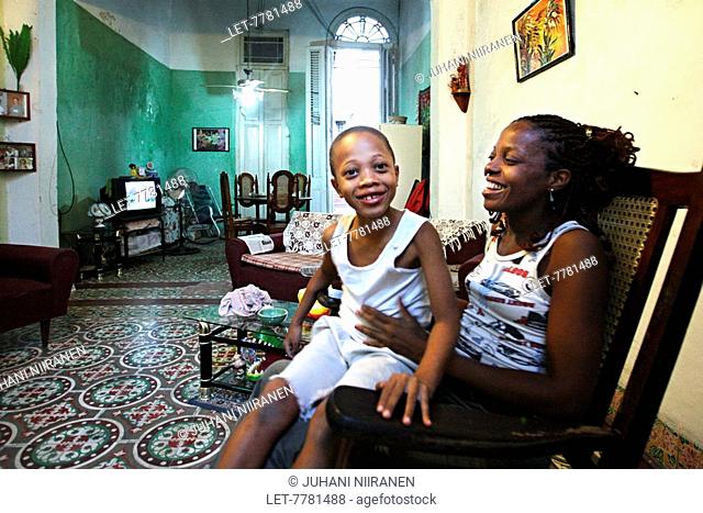 A boy sits in his mother's lap in an apartment in Havana, Cuba. They live in the same apartment with her mother and brother