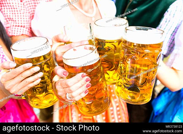 Clinking glasses with beer in Bavarian beer garden, close-up on five beer glasses