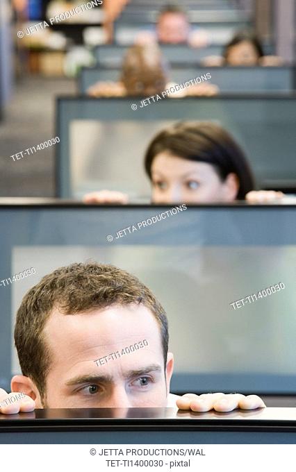 Businesspeople peeking over cubicle walls