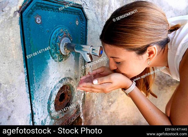 Close up of young woman hydrates herself from a fountain during a heat wave in the city