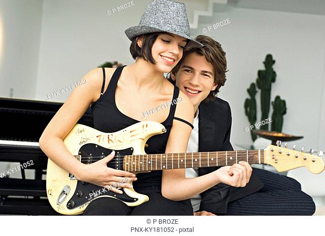 Young woman playing a guitar with a teenage boy leaning beside her