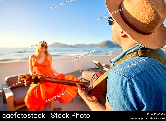 Happy couple playing guitar and dancing on sunny patio with ocean view
