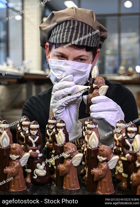 02 December 2020, Brandenburg, Hornow: Anne Walter, chocolatier from the Confiserie Felicitas, decorates small Christmas figures with a mouth and nose protector...
