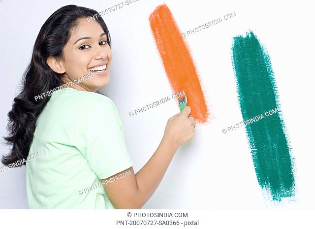 Portrait of a young woman painting a wall with a paintbrush and smiling