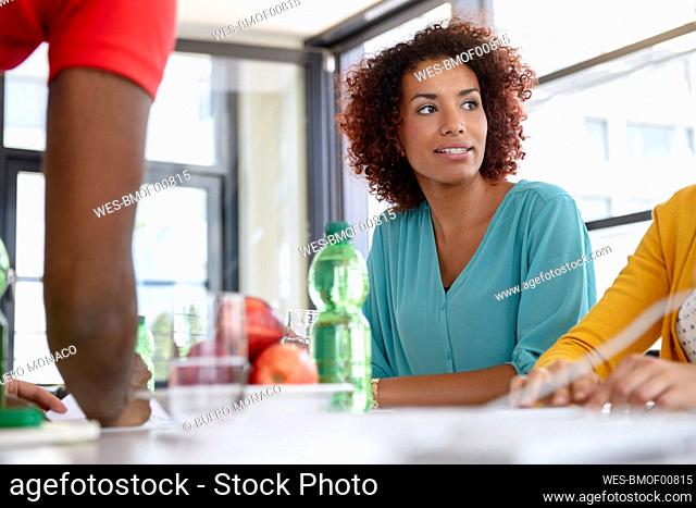 Woman looking away while discussing with colleagues in office