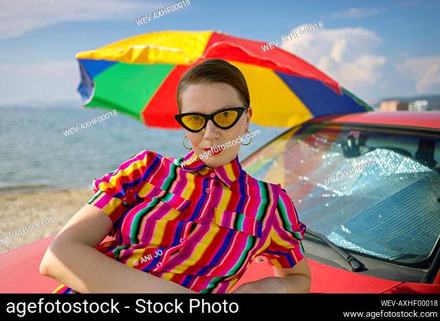 Attractive woman leaning on car at beach during sunny day