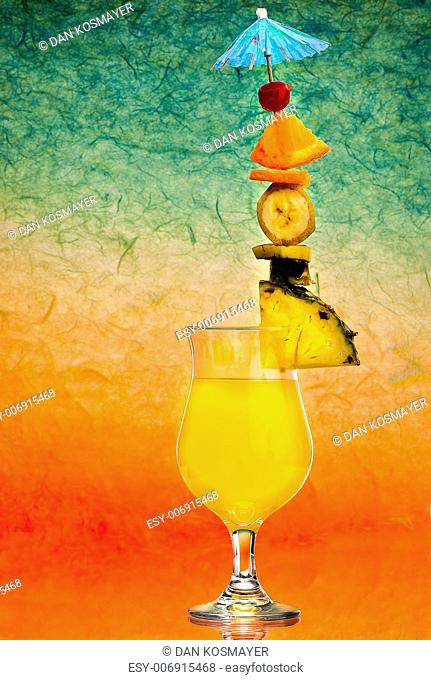 An orange drink with a tower of citrus fruits including a blue umbrella against an abstract sunset colored background